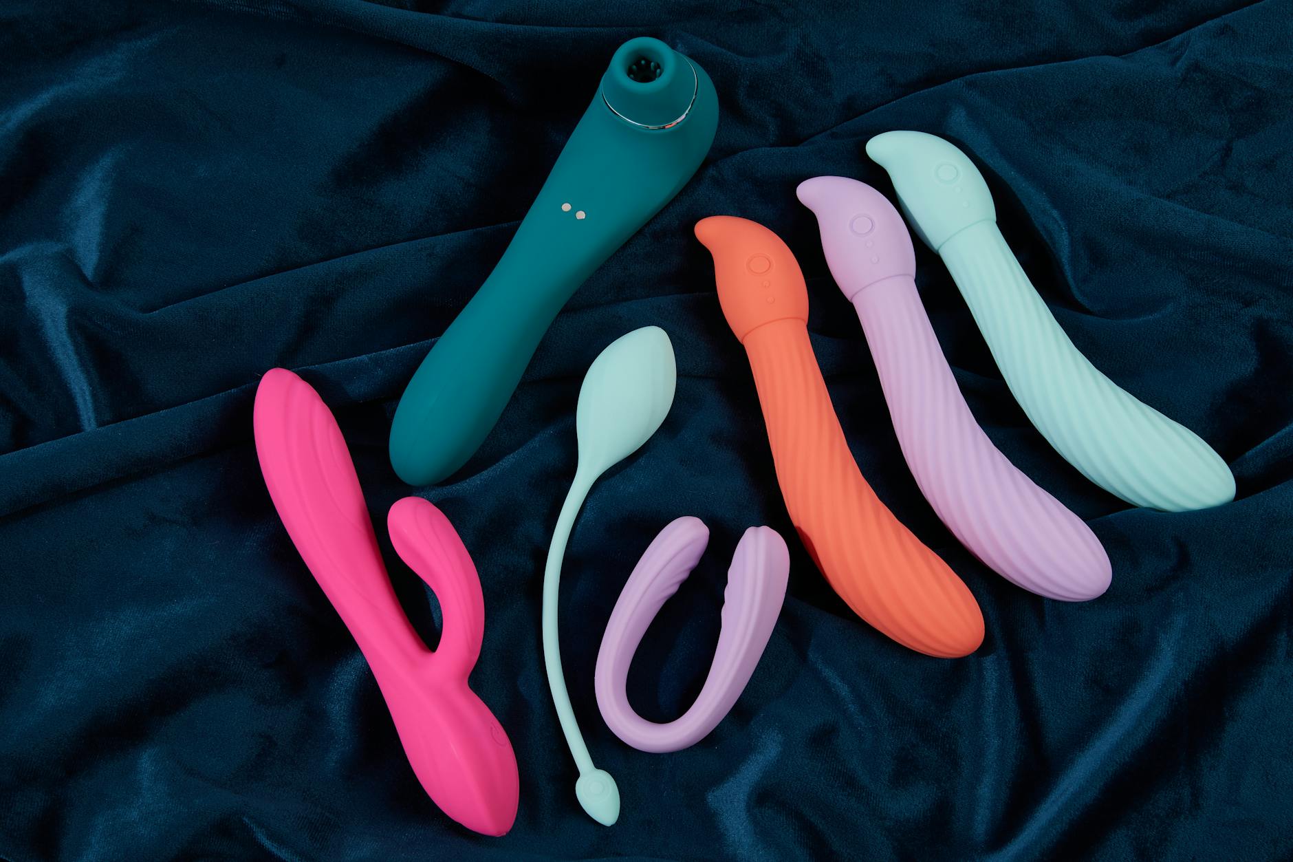 Hand reaching over a variety of colorful clitoral vibrators arranged thoughtfully on a table