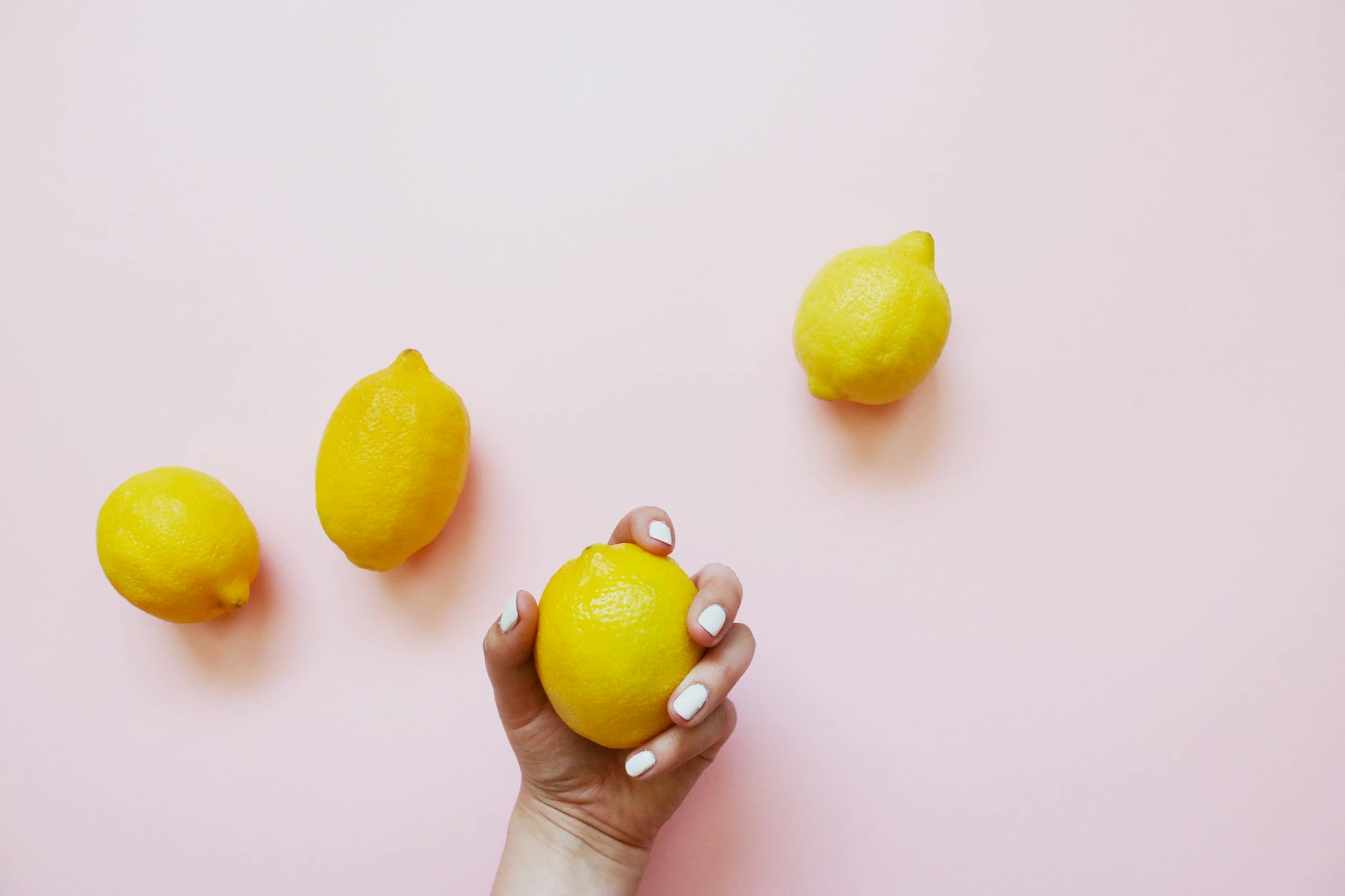 A hand holding a fresh lemon on a soft pink background, symbolizing natural pleasure and renewal