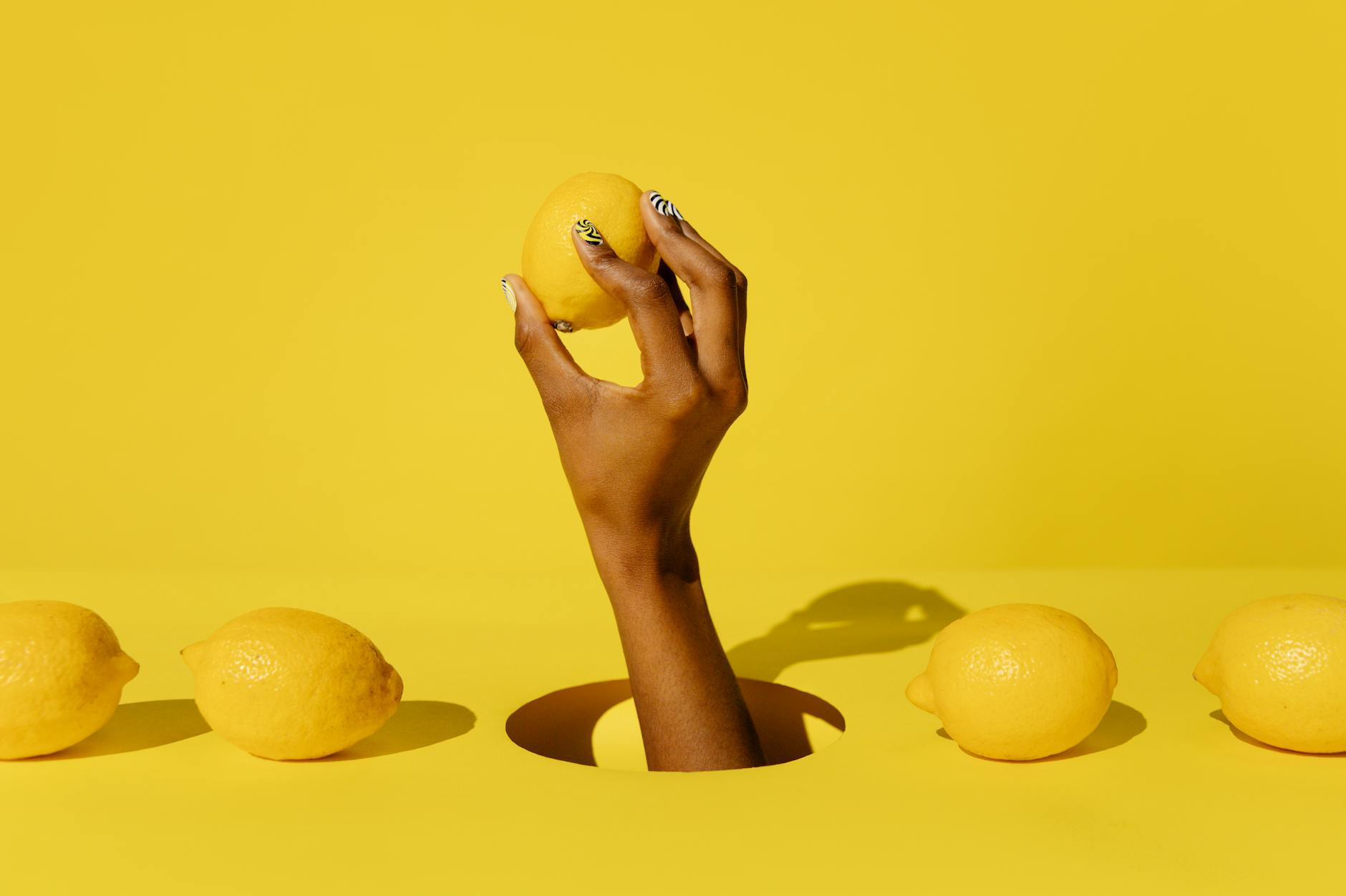 Hand holding a fresh lemon against a yellow background, symbolizing vitality and the refreshing sensation of lemon vibrators