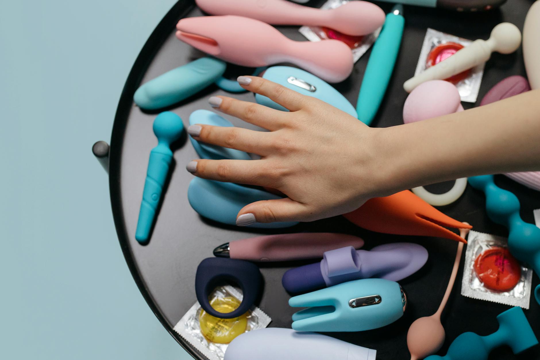 A hand reaching over a variety of colorful adult toys arranged on a table, symbolizing pleasure options and exploration