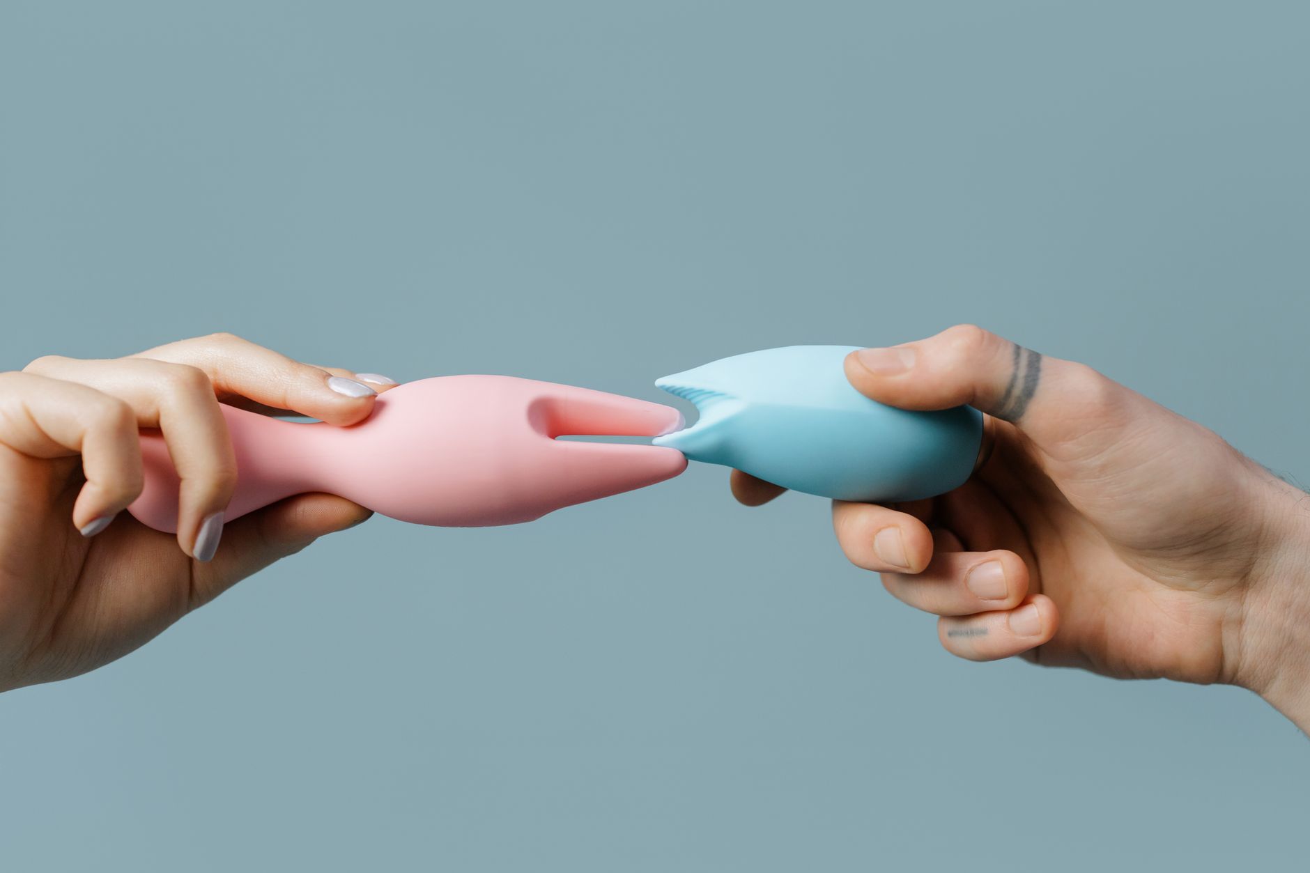 Hands holding pastel-colored silicone vibrators and adult toys for pleasure and intimacy