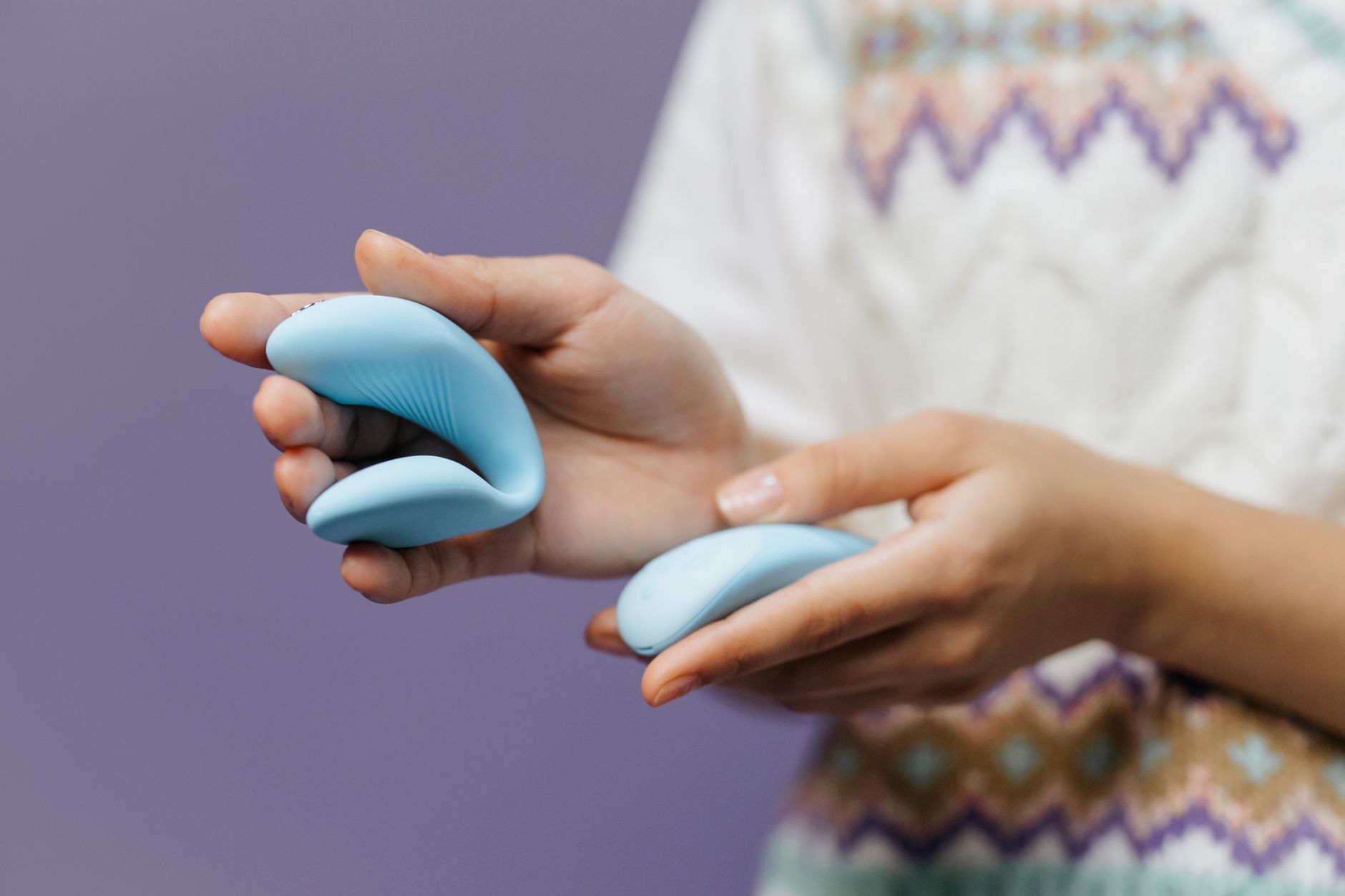 Hands holding a sleek adult toy against a purple background