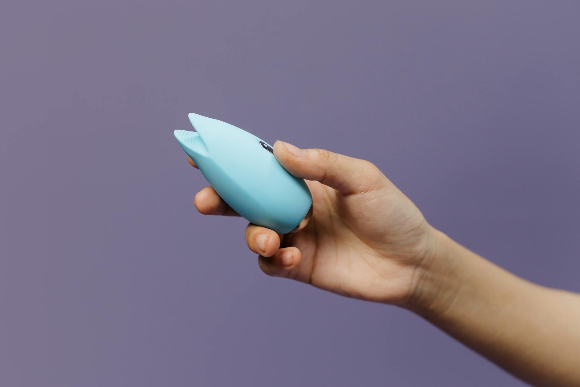 A blue silicone sex toy held gently in hand against a soft purple background, symbolizing the return to self-care after loss.