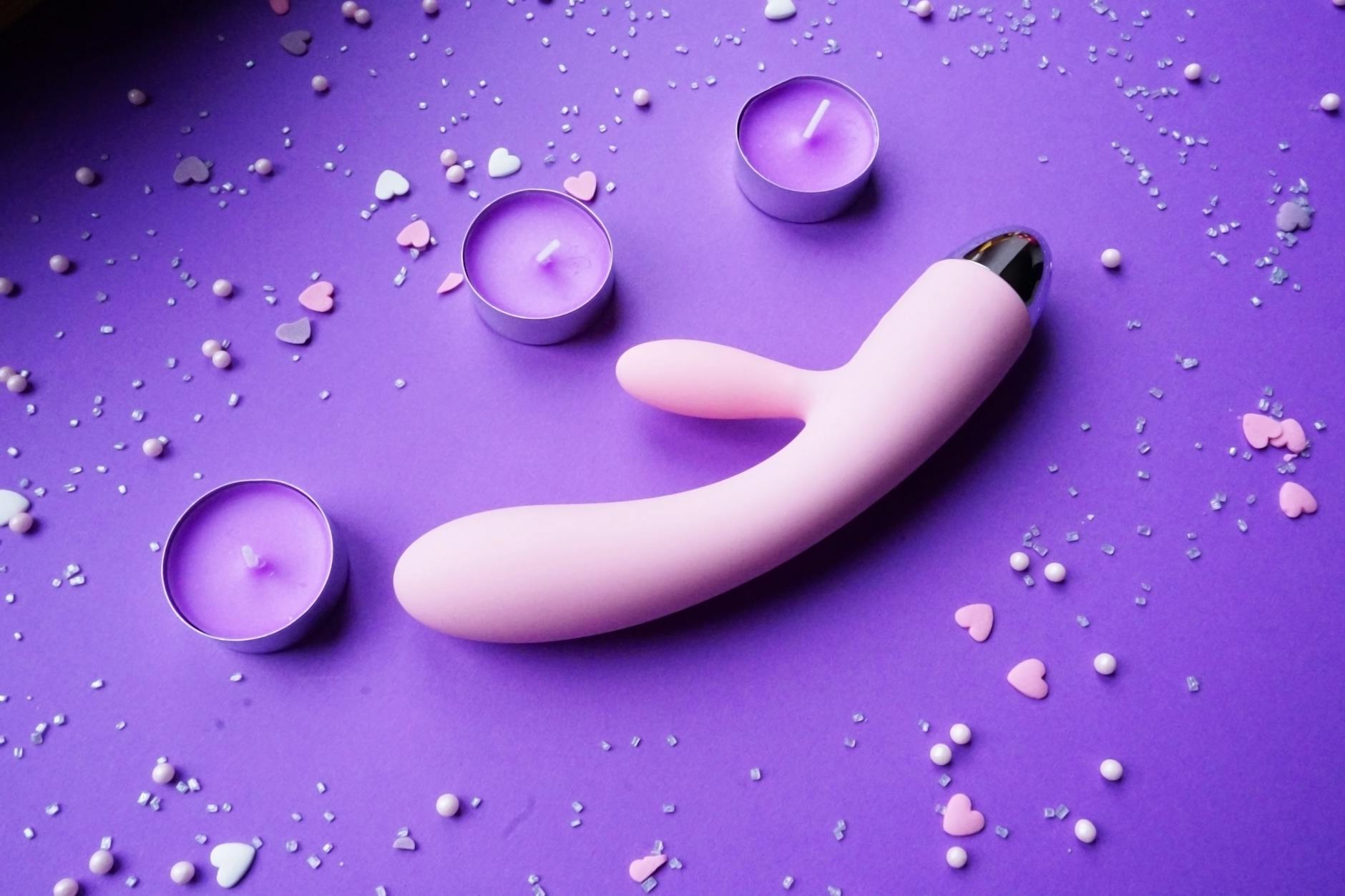 Pink vibrator on a purple background with heart confetti and candles for a romantic setting